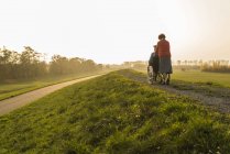 Femme âgée poussant mari en fauteuil roulant dans la nature — Stock Photo