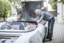 Avô e neto restaurando um carro juntos e olhando para a câmera — Fotografia de Stock