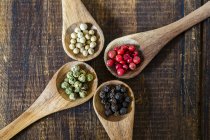 Elevated view of four wooden spoons of different peppercorns on wooden surface — Stock Photo