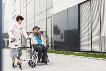 Senior woman with wheeled walker and senior man in wheelchair on pavement — Stock Photo