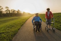Smiling senior couple with wheelchair and wheeled walker on a path — Stock Photo