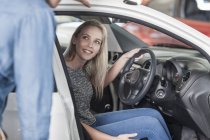 Casal jovem examinando carro novo na concessionária de automóveis — Fotografia de Stock