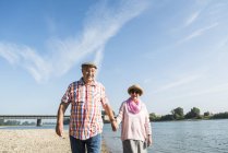 Heureux couple d'aînés marchant main dans la main au bord de la rivière — Photo de stock