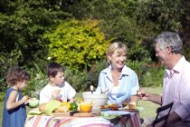 Little boy and girl with their grandparents sitting at dining table in the garden — Stock Photo