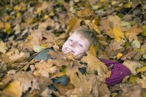 Retrato del niño sonriente tumbado en el suelo cubierto de hojas de otoño - foto de stock