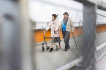 Senior couple walking with walking stick and wheeled walker — Stock Photo