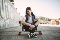 Portrait of serious looking young man sitting on his longboard — Stock Photo