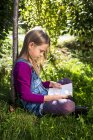 Kleines Mädchen sitzt im Garten und liest Buch — Stockfoto