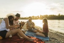 Freunde entspannen am Flussufer bei Bier und Gitarre bei Sonnenuntergang — Stockfoto