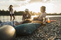 Freunde entspannen sich am Flussufer bei Sonnenuntergang mit Kieselsteinen — Stockfoto