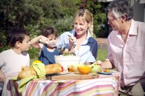 Ragazzino e ragazza con i nonni seduti a tavola in giardino — Foto stock