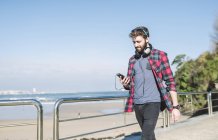 Хипстер с наушниками с использованием смартфона на набережной — стоковое фото