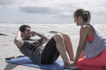Jeune homme et femme faisant de l'exercice sur la plage — Photo de stock