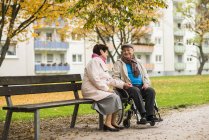 Seniorin sitzt neben Mann im Rollstuhl auf Bank — Stockfoto
