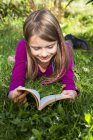 Happy girl lying on grass and reading book — Stock Photo