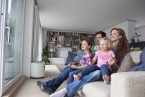 Couple and two little girls sitting on couch in the living room looking through terrace door — Stock Photo