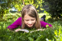 Girl lying on grass in garden and reading book — Stock Photo