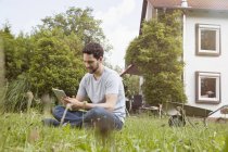 Homem sentado no jardim usando tablet digital — Fotografia de Stock