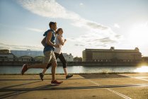 Young couple running by the riverside in city — Stock Photo