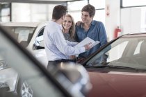 Revendeur automobile montrant la brochure au jeune couple dans la salle d'exposition — Photo de stock