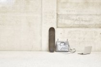 Скейтборд, сумка и ноутбук у бетонной стены — стоковое фото