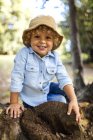 Портрет усміхнений блондин маленький хлопчик капелюсі, сидячи на мертву деревину — стокове фото