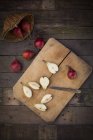 Whole and sliced organic red Clapp Favourites, wooden board and kitchen knife on dark wood — Stock Photo