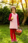 Kleines Mädchen steht mit Weidenkorb voller Äpfel auf einer Wiese — Stockfoto