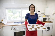 Smiling woman holding tray of freshly baked cookies — Stock Photo