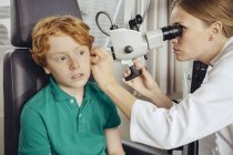 Doctora examinando a un niño pequeño con microscopio - foto de stock