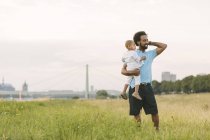 Happy african american father carrying his son in field — Stock Photo