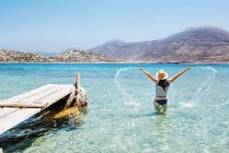 Grecia, Isole Cicladi, Amorgos, Donna che spruzza nelle acque blu del Mar Egeo vicino a un molo di legno — Foto stock