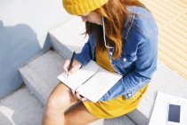 Jovem mulher sentada em passos escrevendo algo — Fotografia de Stock
