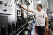 Homem pressionando botão na fábrica de engarrafamento de cerveja — Fotografia de Stock