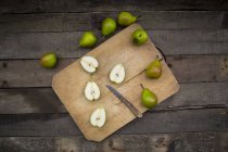 Whole and sliced pears with kitchen knife on wooden board — Stock Photo
