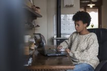 Jeune femme assise au bureau à la maison avec ordinateur portable — Photo de stock