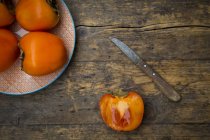 Whole and sliced kaki persimmons and a kitchen knife — Stock Photo