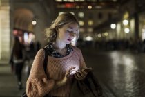 Jeune femme utilisant un smartphone dans la rue le soir — Photo de stock