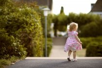 Back view of blond little girl wearing dress with floral design — Stock Photo