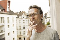 Retrato del hombre fumando en el balcón mirando a la cámara - foto de stock