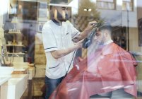 Парикмахерская высушивает волосы клиента за окном парикмахерской — стоковое фото