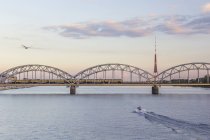 Lettonia, Riga, ponte ferroviario e torre TV al fiume Daugava la sera — Foto stock