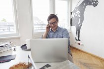 Lächelnder junger Geschäftsmann mit Laptop und Handy in einem modernen Büro — Stockfoto