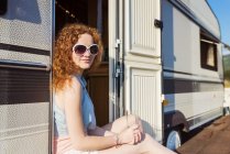 Portrait of smiling young woman sitting at entrance of caravan — Stock Photo
