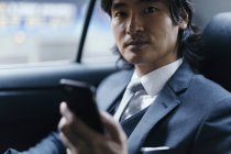 Retrato del hombre de negocios en el asiento trasero del coche con teléfono celular - foto de stock