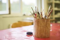 Mug with paintbrushes and tools over table — Stock Photo