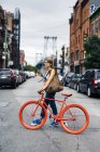 Estados Unidos, Ciudad de Nueva York, Williamsburg, mujer con bicicleta roja de carreras cruzando la calle - foto de stock
