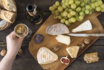 Bandeja de queso con camembert, queso de nuez, gorgonzola, taleggio y copa de champán de mano masculina - foto de stock