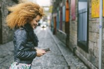 Donna sorridente con i capelli afro guardando il suo smartphone — Foto stock