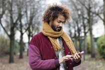 Retrato de homem com argolinhas tingidas usando cachecol usando seu smartphone — Fotografia de Stock